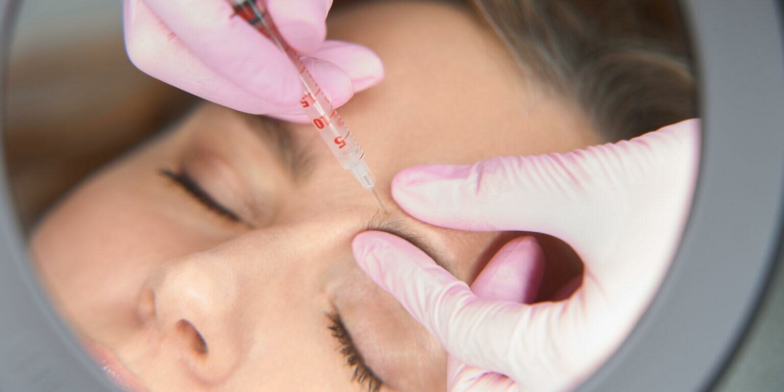 Doctor esthetician makes beauty injections to a blonde woman, the process of the injection procedure is reflected in the mirror